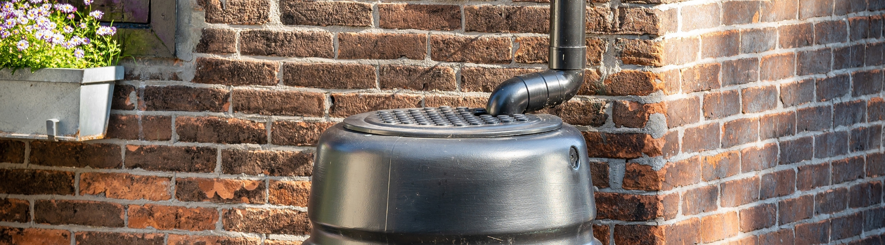 A black rain barrel is sits against the wall of a brick building.