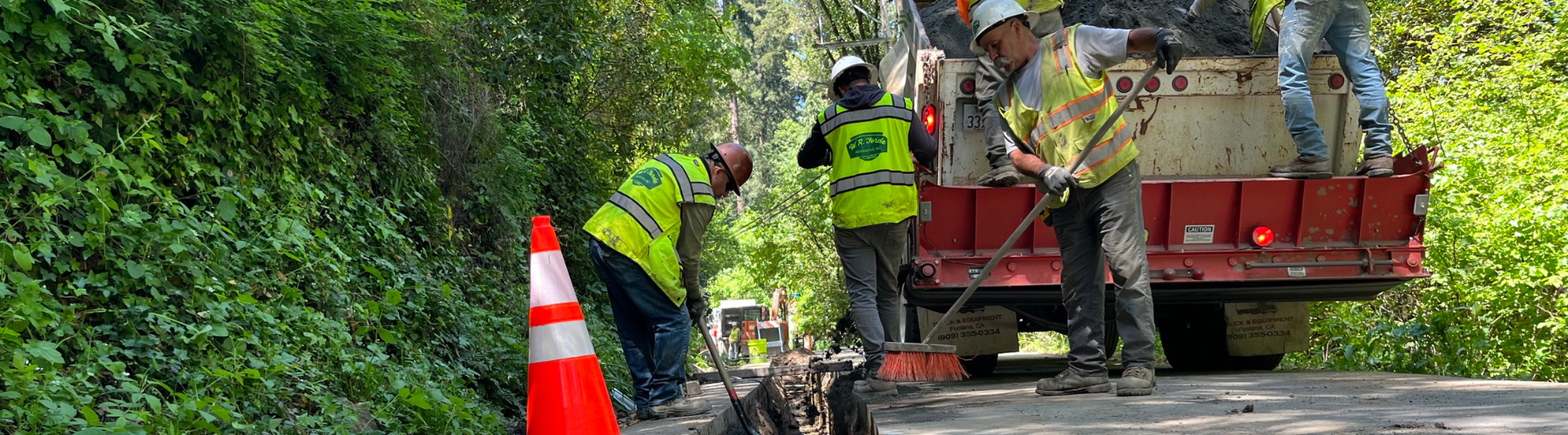 Workers wearing hard hats and safety gear work to fill in a trench.