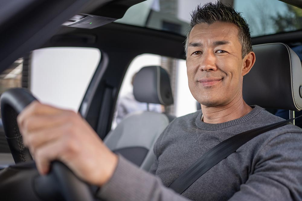 Man smiling and driving in a car with a sunroof