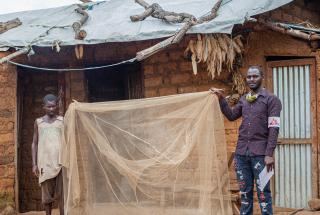 Sibomana Louis, refugiado burundés que vive en el campo de Nduta desde 2015, sostiene el mosquitero que recibió de MSF junto a Fulgence Irakoze, supervisor de control de vectores de MSF.