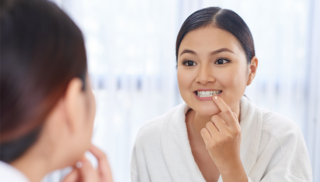 Young woman wearing a robe and examining her teeth in the mirror