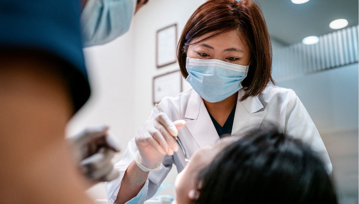 Dentist and her assistant wearing blue face masks examine a patient large