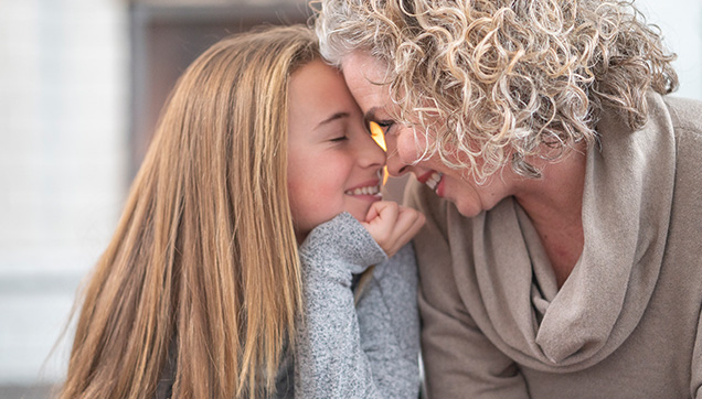 young girl and older woman smile while leaning in close to one another touching foreheads