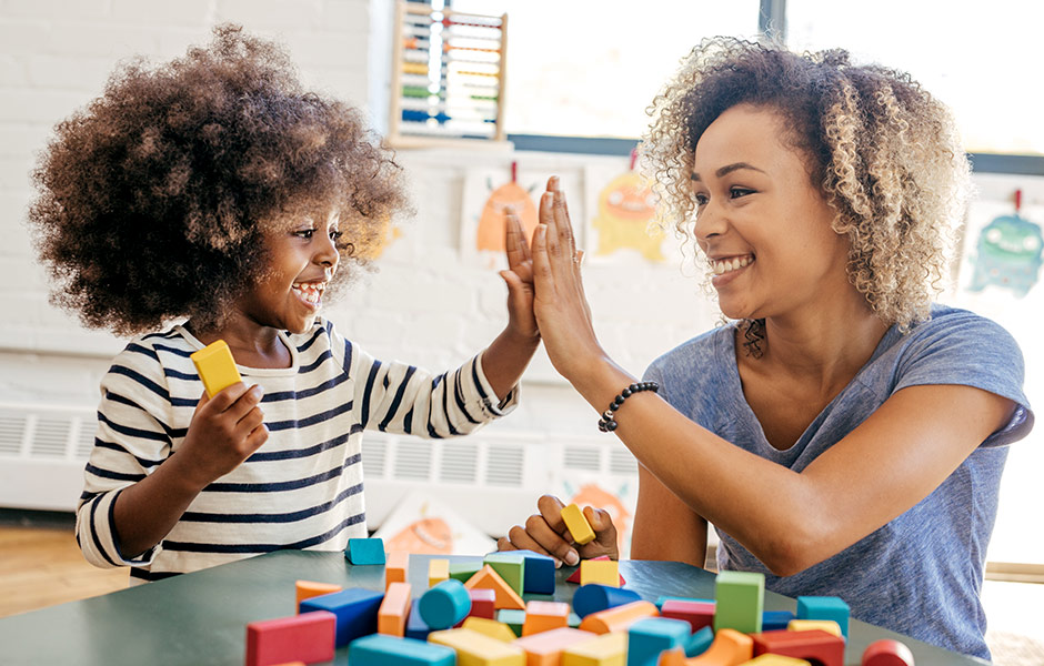 A young student plays with blocks and gives a high-five to a young female teacher. 