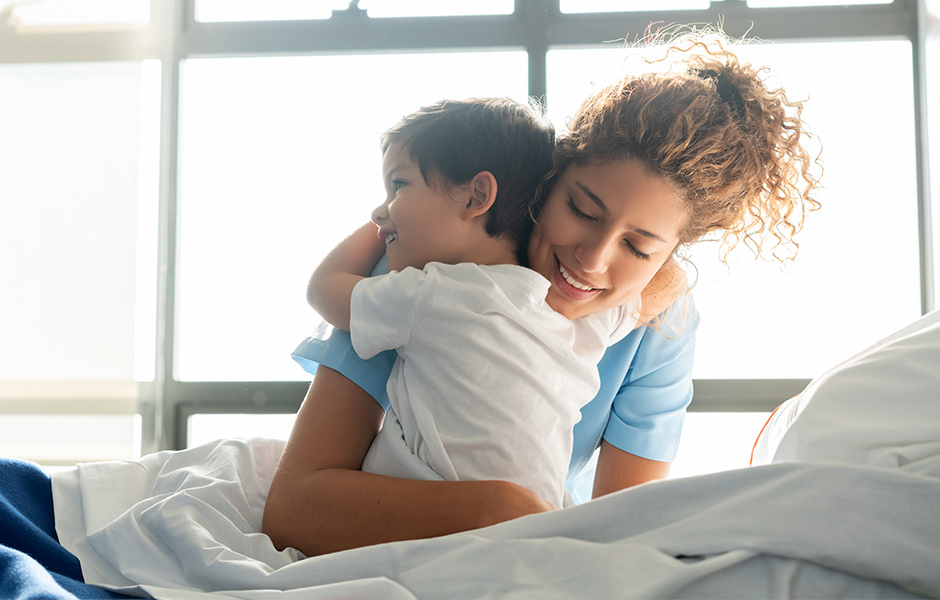 Woman caregiver hugs smiling toddler in a hospital bed