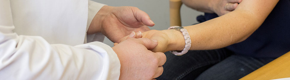 Health care professional examining a person’s hands for signs of scleroderma.