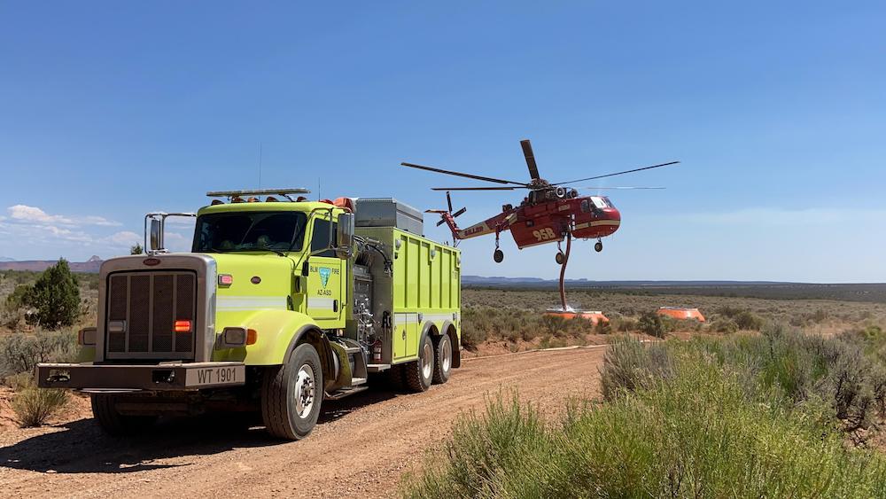 A large helicopter gets water from a tank that is refilled by an engine crew.