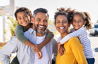 A stock photo of happy parents giving a piggyback ride to their daughters outdoors.