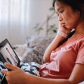 A woman sits in a chair looking at a tablet screen she is holding in her lap. 