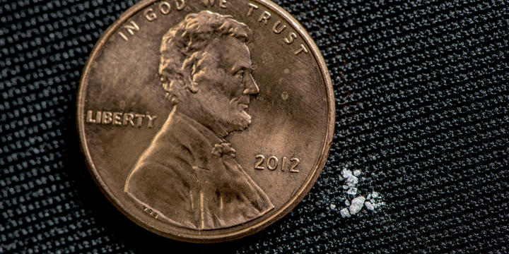 Black background. Photo of a penny. Next to the penny is a tiny amount of a white powder.