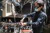 A person wearing safety goggles works at a table of scientific equipment.