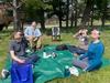 Four people sitting outside on a green tarp wear eclipse glasses as they peer up into the sky. 