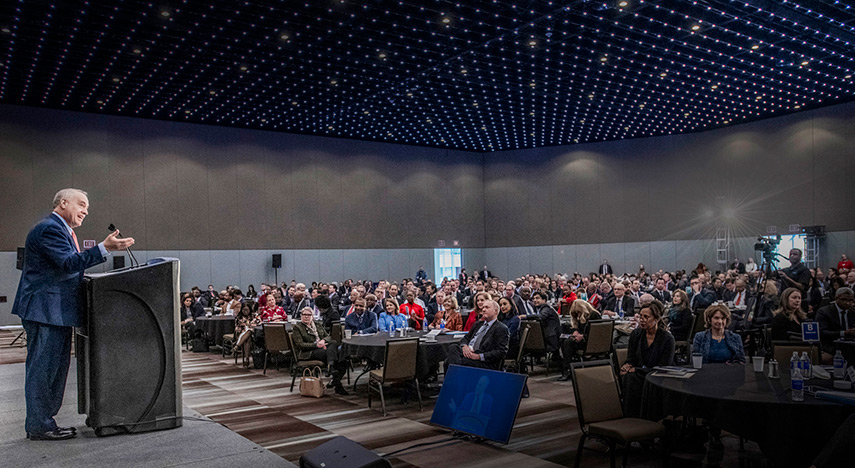 Thomas P. DiNapoli speaking in front of a podium to a a crowd of people in a convention hall. 