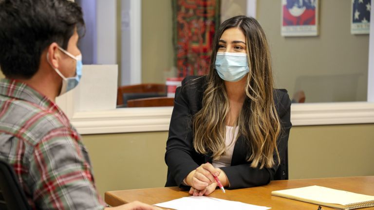 A female student is seated at a desk while wearing a mask