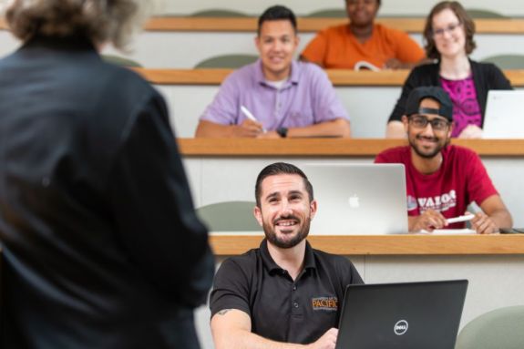 Five students in a classroom listen to a professor teaching