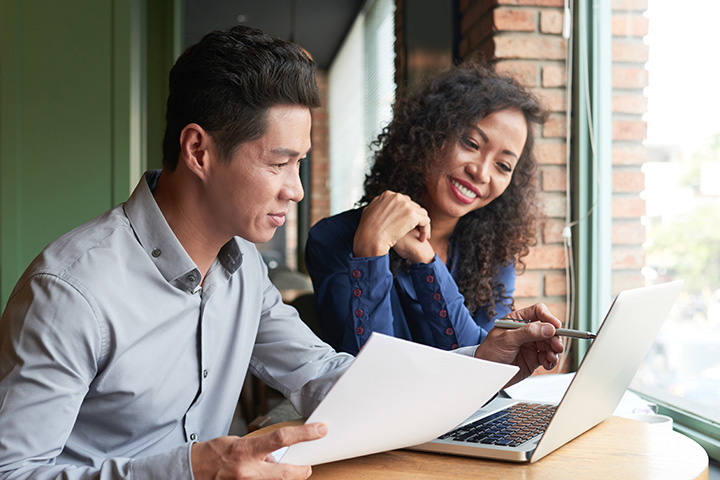 business couple discussing project viewing laptop and printed material