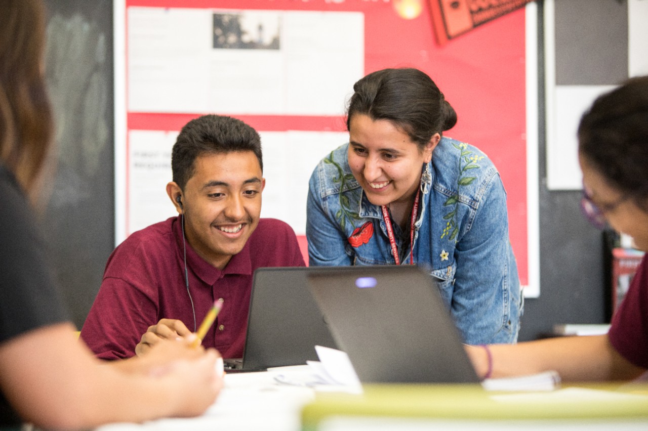 A woman looks over a student's shoulder as he works on a laptop.