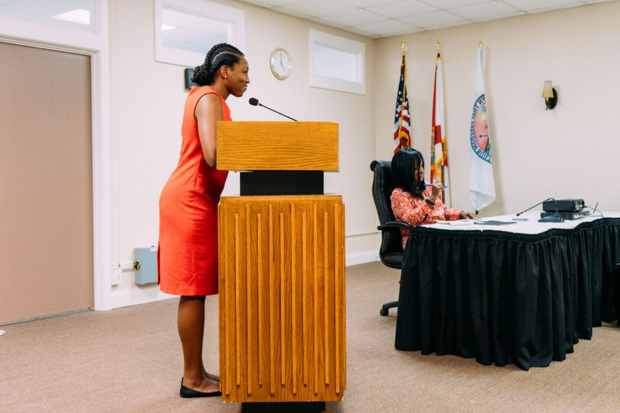 Young woman stands at podium making announcement.