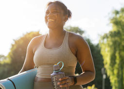 Person holding water bottle and yoga mat smiling