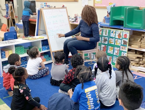 Children sitting on classroom rug listening to teacher at a white board