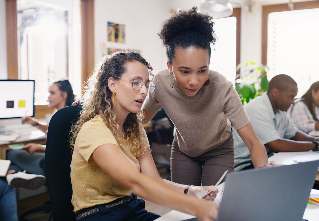 Two women working in an office at a computer discussing a project.