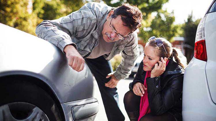 Two people looking at dents on a car in a parking lot.