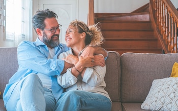 Mature couple embrace on sofa inside home discussing equity release