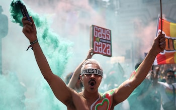 Bare-chested, the young man wears a 'Palestine' visor and holds a smoke flair while another demonstrator behind him holds a sign saying 'Gays for Gaza'