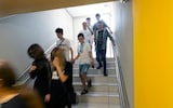 Children walk down a staircase, one smiling and holding hands with a woman who might be his mother