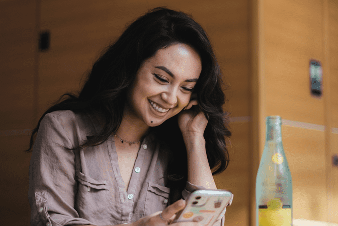 Woman in gray button up shirt reading her phone, with bottle of water next to her.