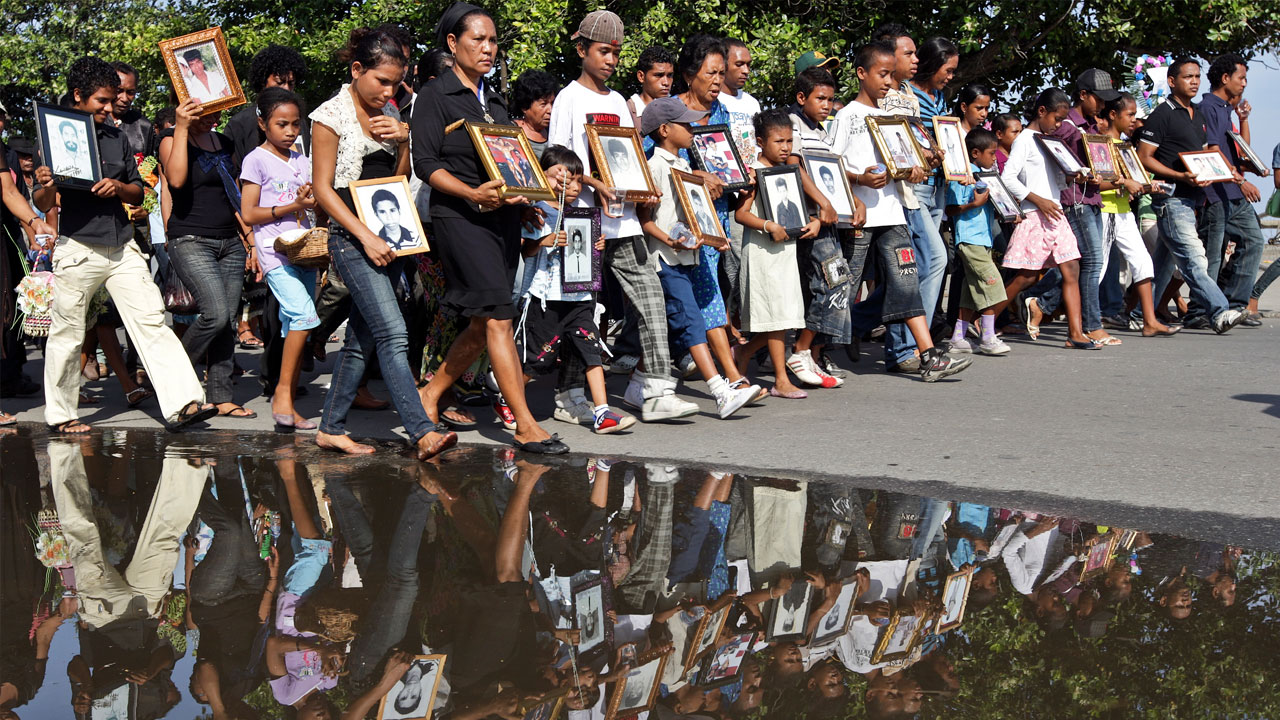 Des familles défilent portant des photos encadrées de victimes.