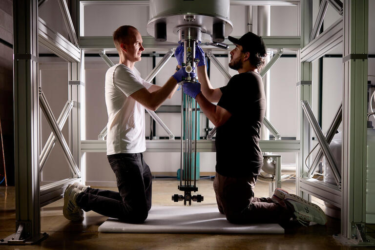 two men kneel on ground to put together lab equipment