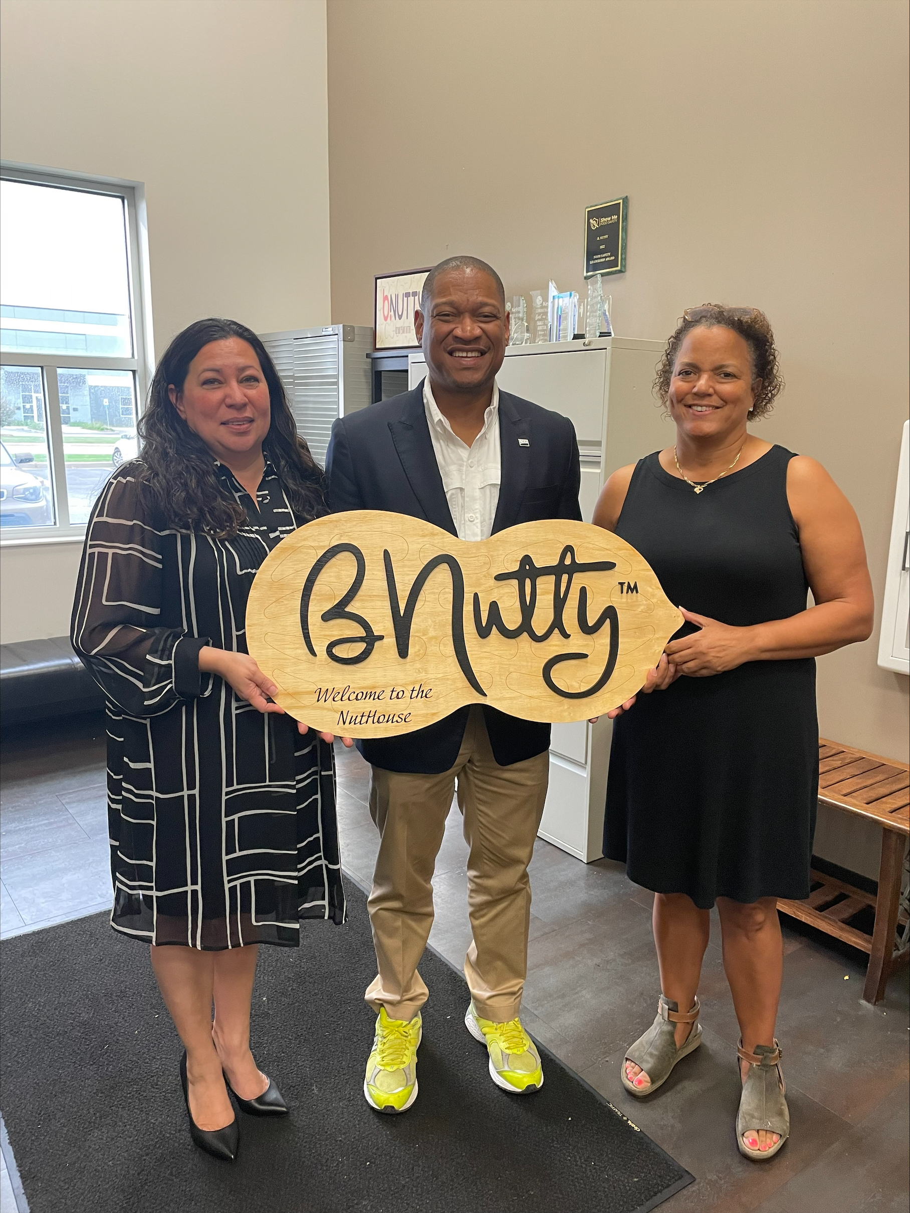 Three people smiling holding a Welcome to the NutHouse sign