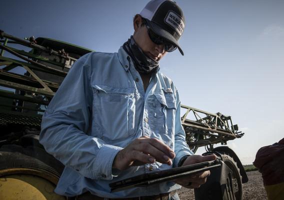 A person using a tablet with a tractor in the background