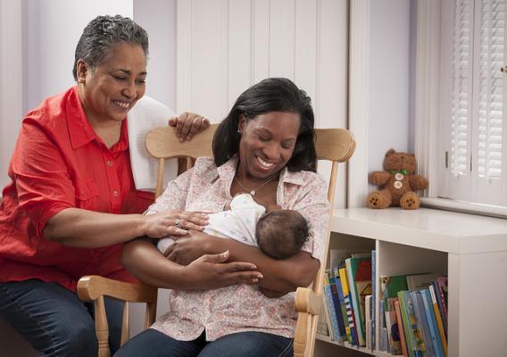 A woman breastfeeding in a chair with another woman beside her