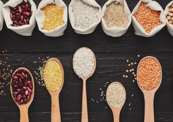 Assorted gluten free grains in cloth bags and spoons on rustic wooden background, top view