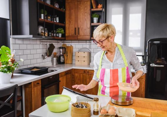 A middle-aged woman cooking in the kitchen using a recipe from her tablet