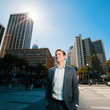 Student walks down the street with SF skyline behind him.