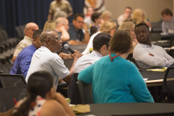 People sitting together listening to a person speaking through a microphone