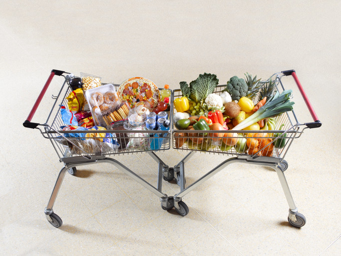 2 metal shopping carts, one filled with ultraprocessed foods and one filling with colorful, healthy fruits and vegetables