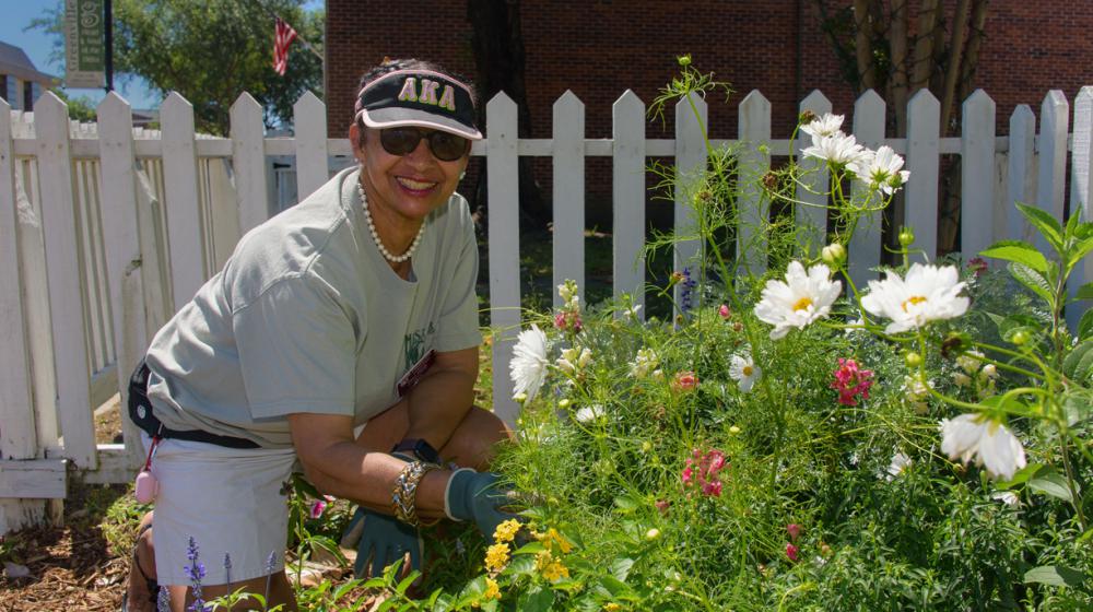 A woman kneels next to a bed of flowers.