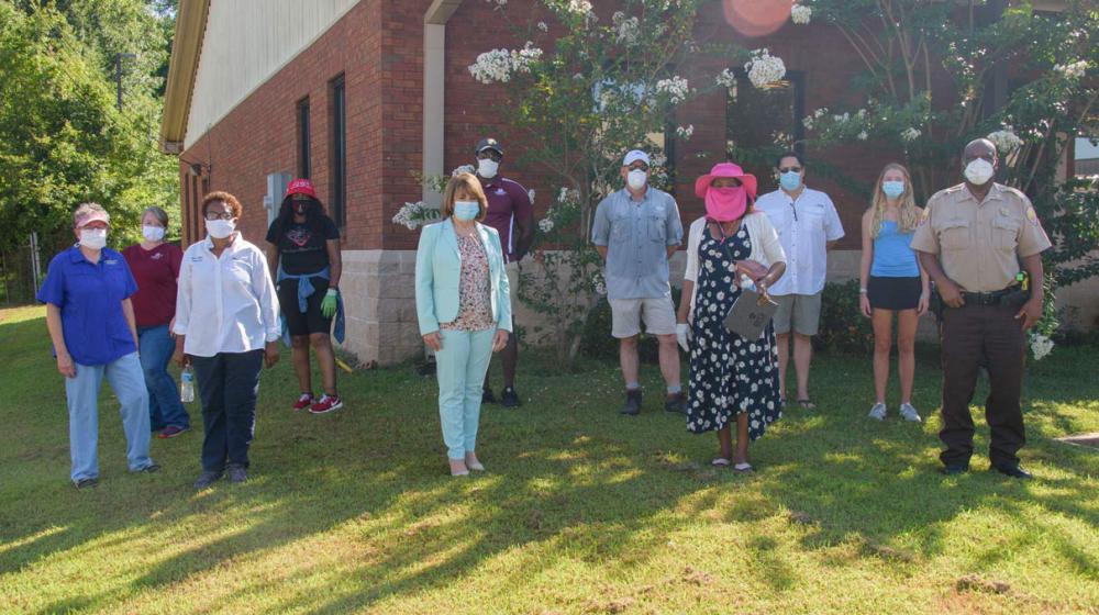 A group of 11 men and women wearing masks stand in front of a brick building.