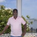 A man stands on a porch with a white crepe myrtle behind him and the Mississippi River and bridge in the distance.