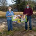 A man and woman wearing masks hold each side of a banner that reads “2020 Winner $2,500.”