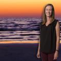 A woman, smiling, standing in front of the ocean