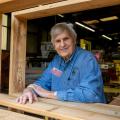 A man wearing a denim shirt and a Master Gardener nametag smiling with a table frame around him listing #1,000 on wood.