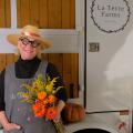 A woman with a straw hat and round-framed glasses holding a bunch of flowers and smiling.