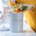 A woman scrapes vegetable scraps off a cutting board into a countertop compost bin.