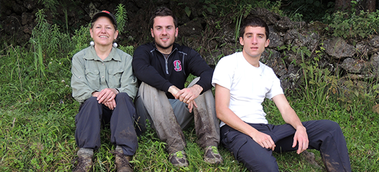 Susan and her two sons sit on a grassy hill for a family photo