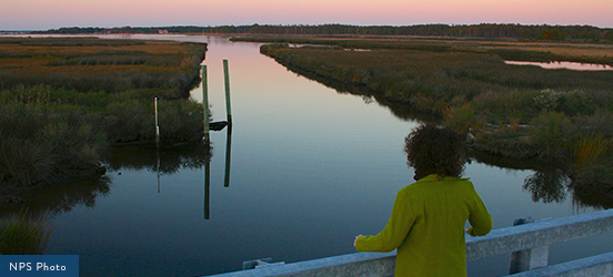 A woman stands on a bridge overlooking streams and wetlands at sunset at Harriet Tubman Underground Railroad National Historical Park